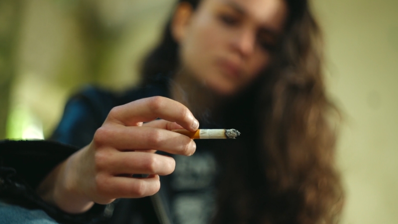 Close-up of a young woman holding a lit cigarette, representing substance use