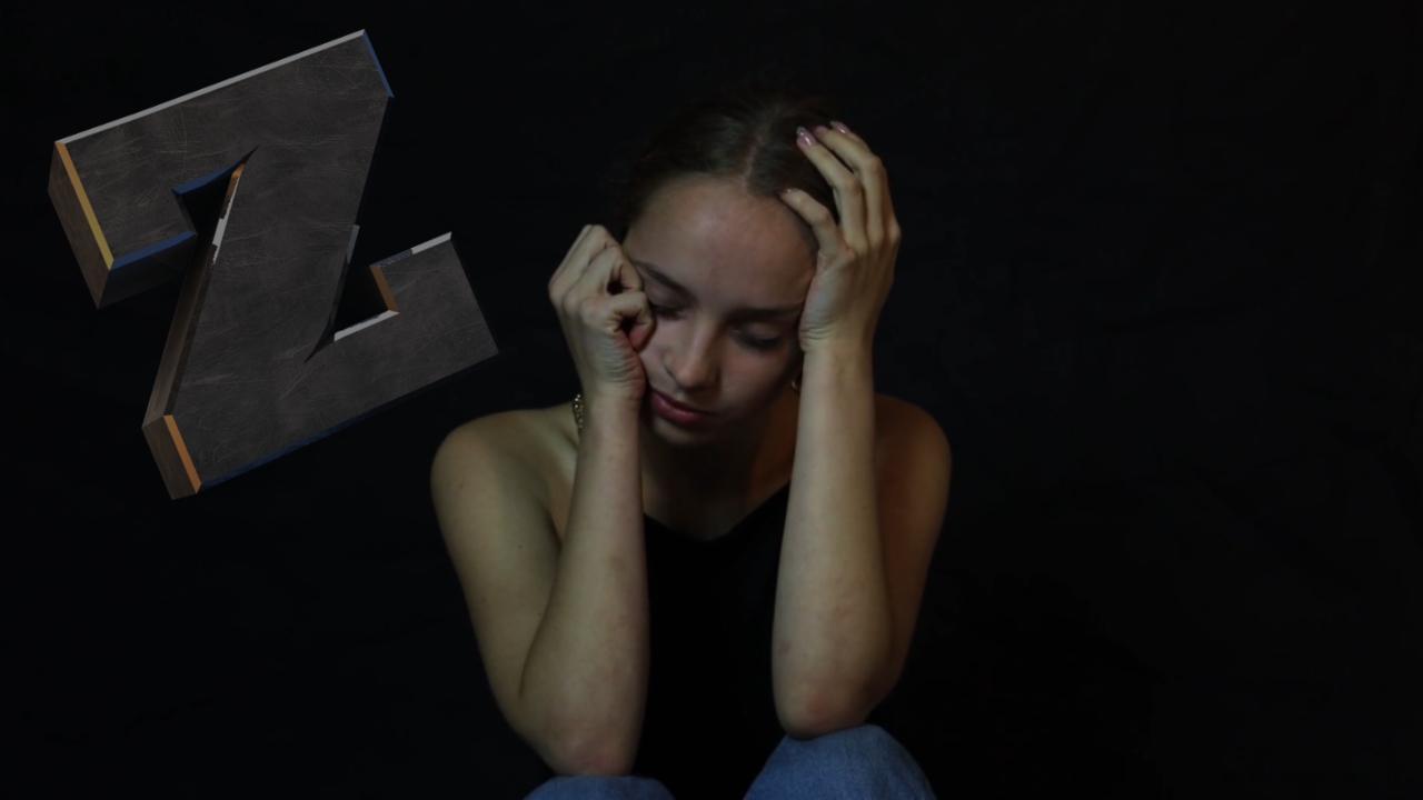 Young woman sits with head in hands in a dark setting, representing emotional distress among Gen Z