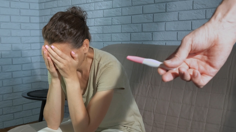 Woman looking distressed while another person holds a negative pregnancy test in the foreground
