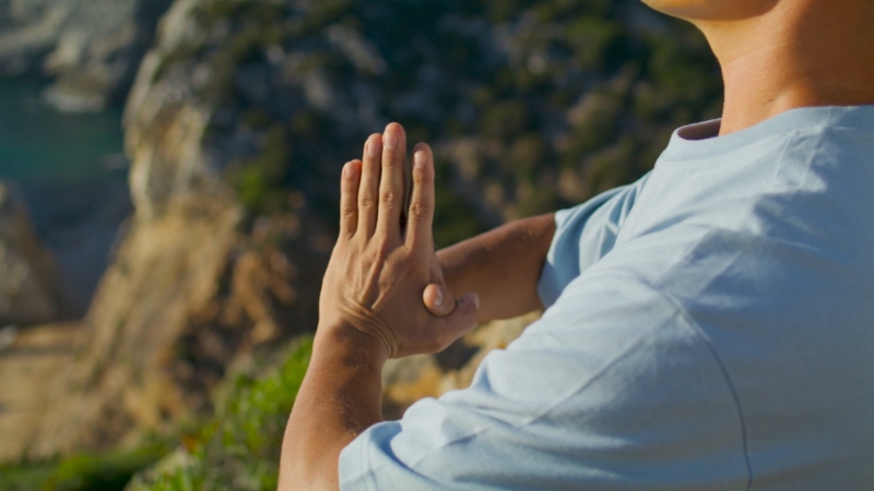 Person sitting outdoors with hands pressed together during meditation practice