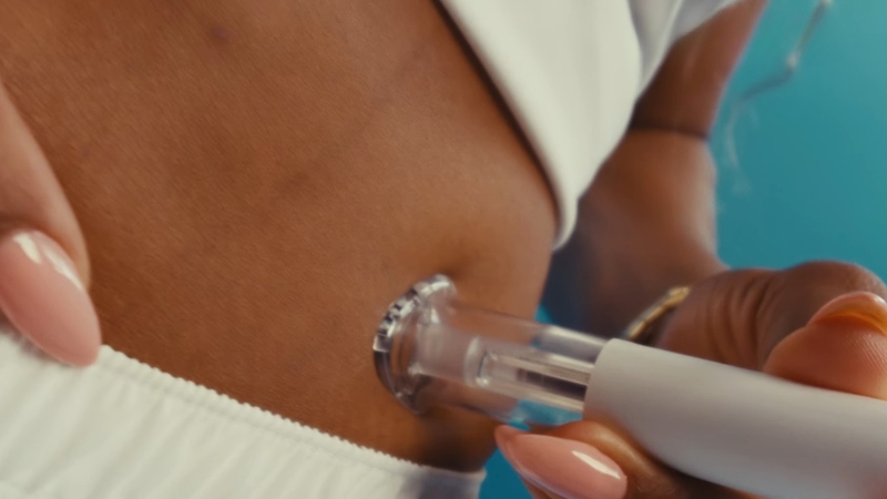 Close-up of a GLP-1 injection pen pressed against a person’s abdomen