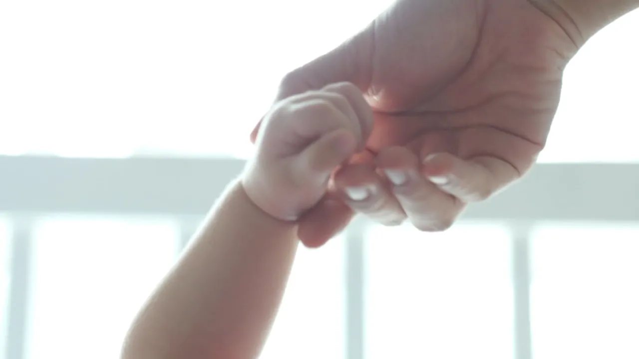 Close-up of a baby holding an adult’s finger, illustrating US births and family life