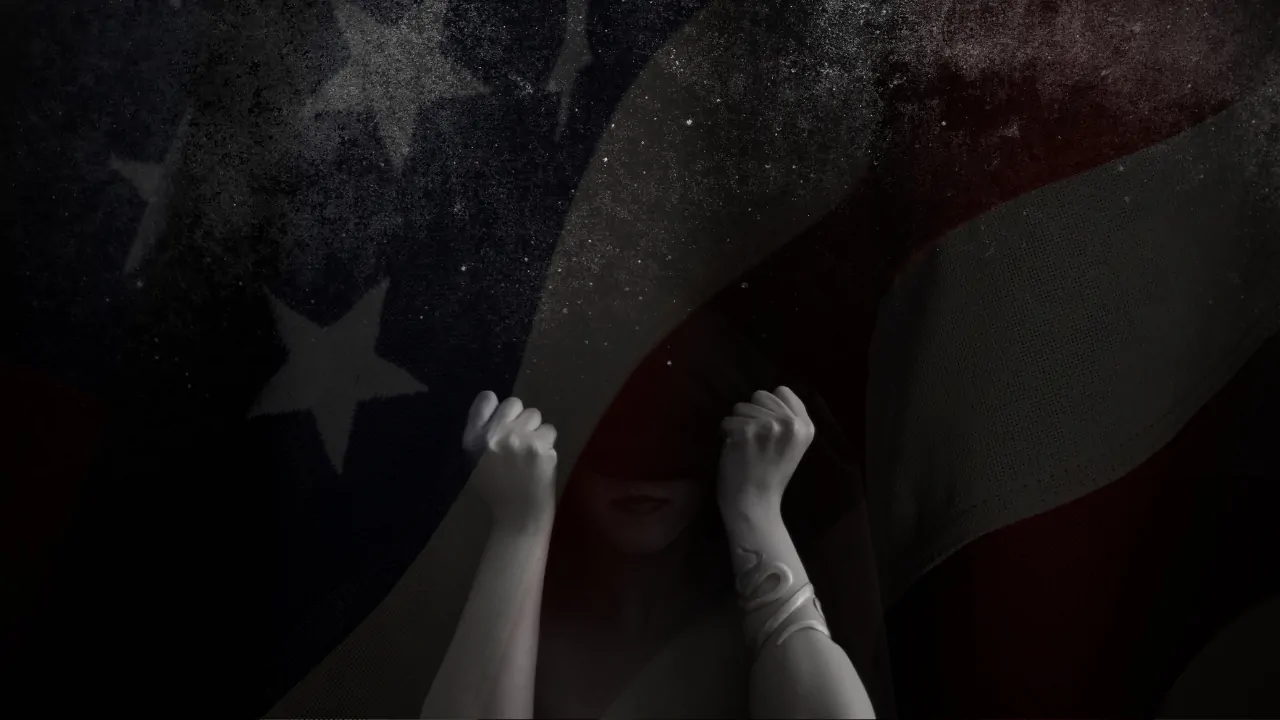 Person sits in shadow with fists raised beneath a dark American flag, symbolizing distress linked to US suicide rates