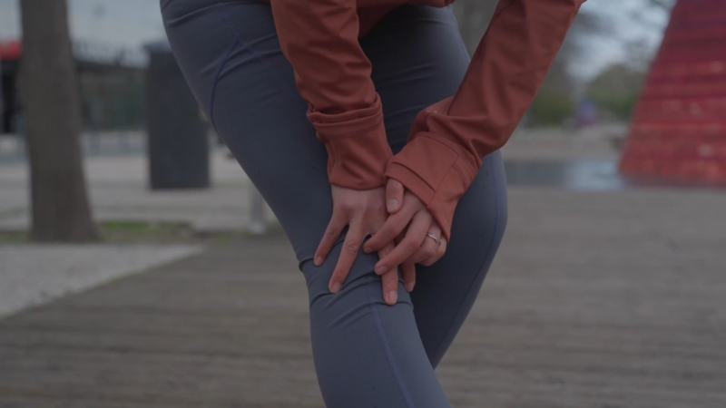 Woman holding her knee outdoors, showing joint pain related to osteoarthritis
