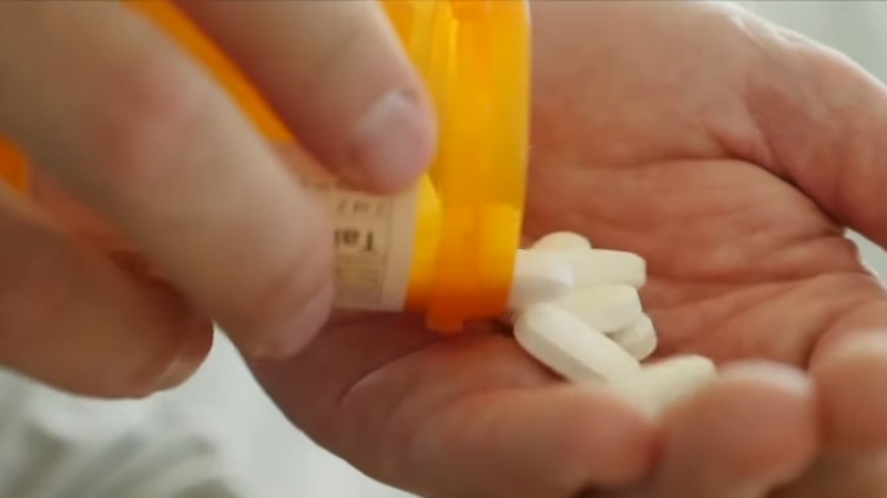 A person pours prescription pills from an orange bottle into their hand