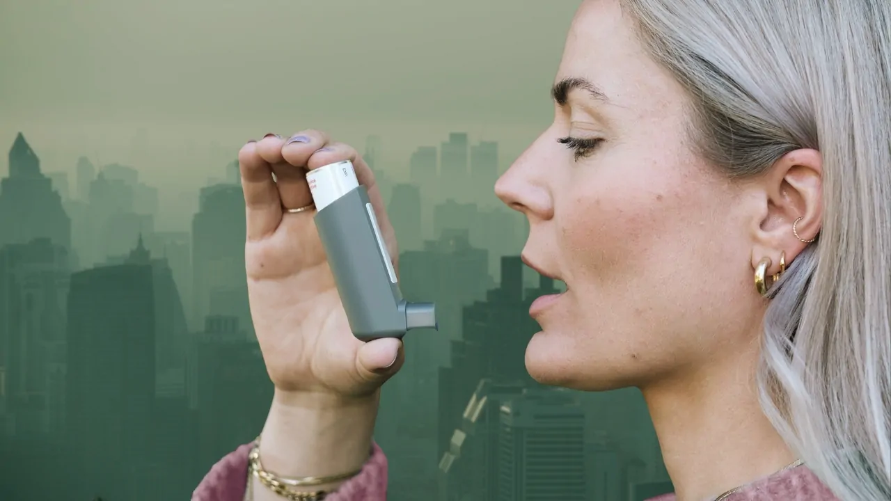Woman using an inhaler in a smoggy city, highlighting air quality and asthma hospitalizations