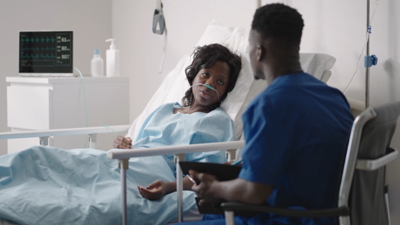 Patient receiving oxygen in a hospital bed while speaking with a doctor