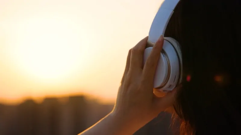 Person wearing headphones at sunset, listening to music outdoors