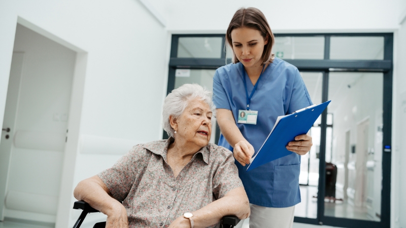 Nurse reviews paperwork with an elderly patient in a hospital hallway during discharge planning