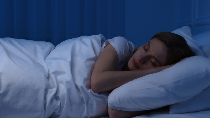 Woman asleep in bed at night under soft blue light