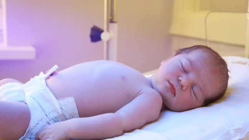 Newborn baby sleeping in a hospital crib with medical equipment nearby