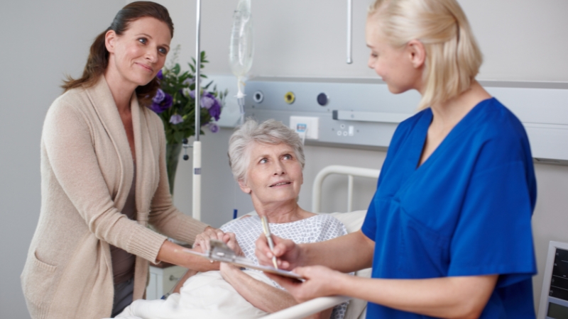 Nurse and family member speak with a patient in a hospital room during the discharge process