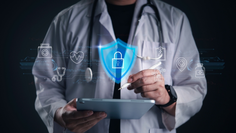 Doctor using a tablet with a digital shield icon that represents hospital cybersecurity protection