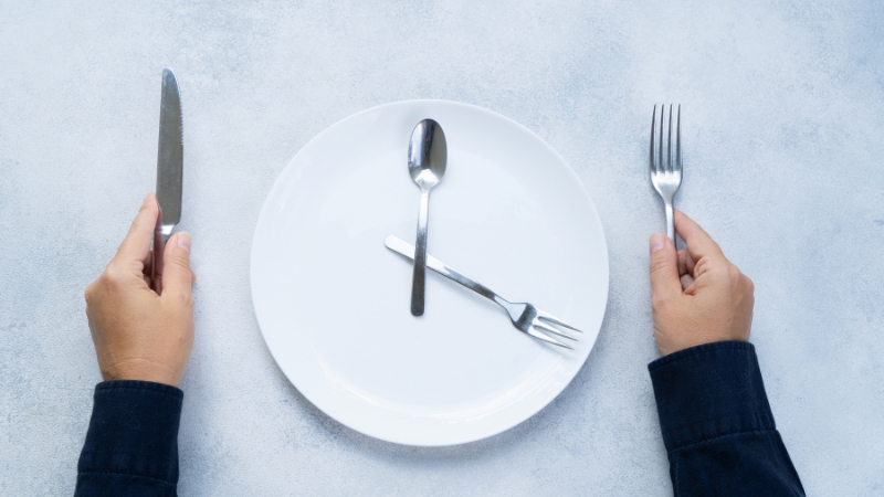 Person holding fork and knife in front of an empty plate
