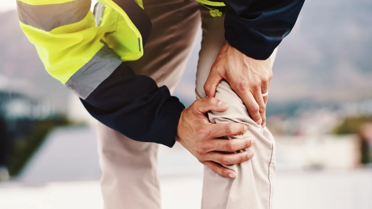 Worker holding a painful knee after a workplace injury while wearing safety gear