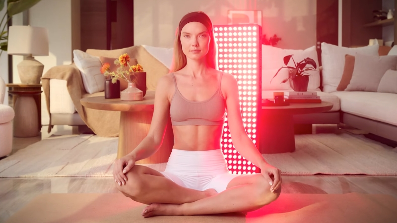 Woman sitting in front of a panel during a near-infrared light therapy session at home