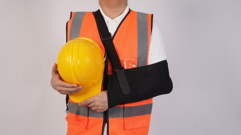 Injured construction worker with an arm sling holding a hard hat