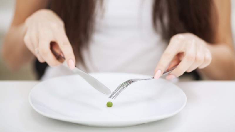 Woman holding fork and knife over an almost empty plate illustrating fasting and autophagy