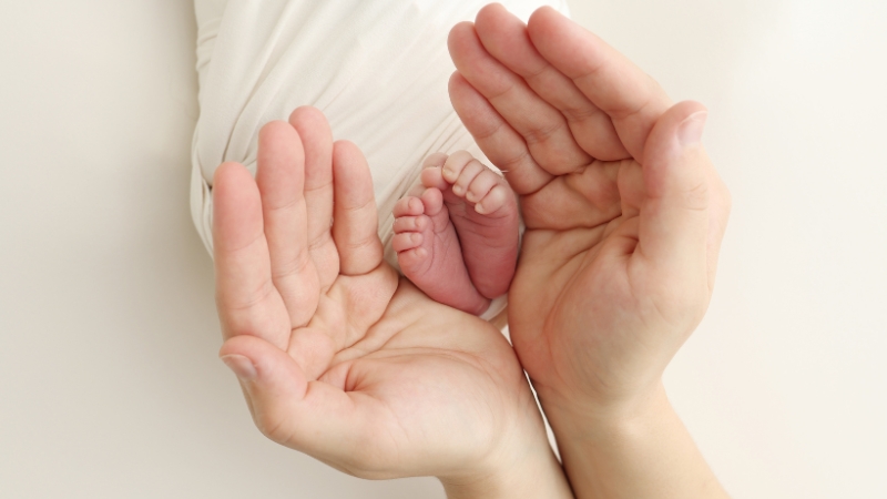 Adult hands gently holding the tiny feet of a newborn baby