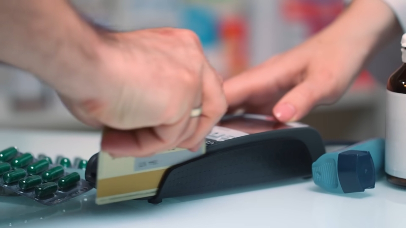 Person paying for medicine with a card, showing rising national health spending