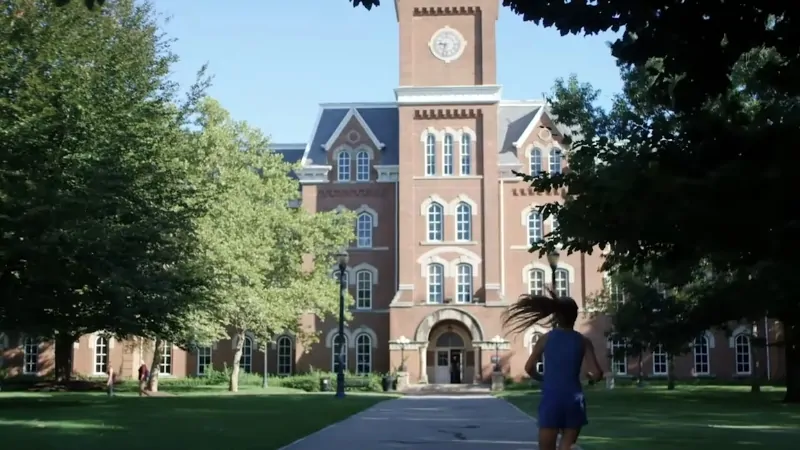Student walking across the Ohio State University campus in front of a historic academic building