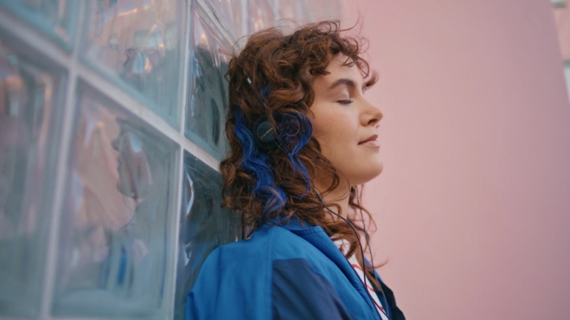 Woman leaning against a wall with headphones, listening to music with eyes closed