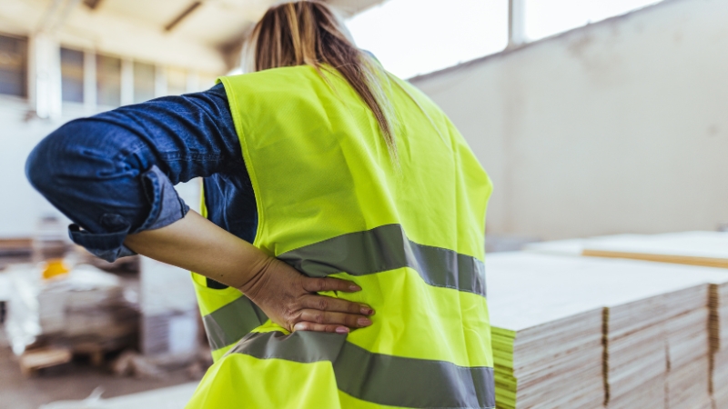 Worker in a safety vest holding her lower back after a workplace injury