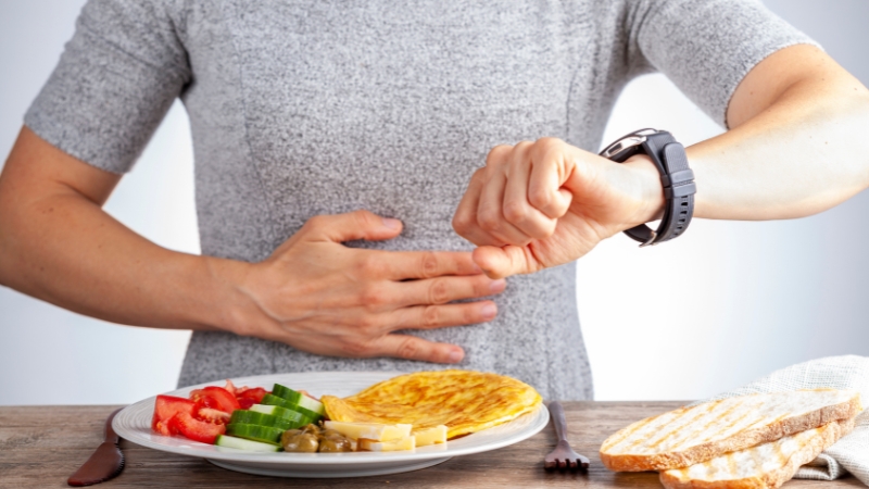 Person checking a watch before eating a meal, illustrating timing and limits of fasting for autophagy research