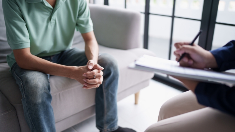 Counselor taking notes during a therapy session with a client seated on a couch