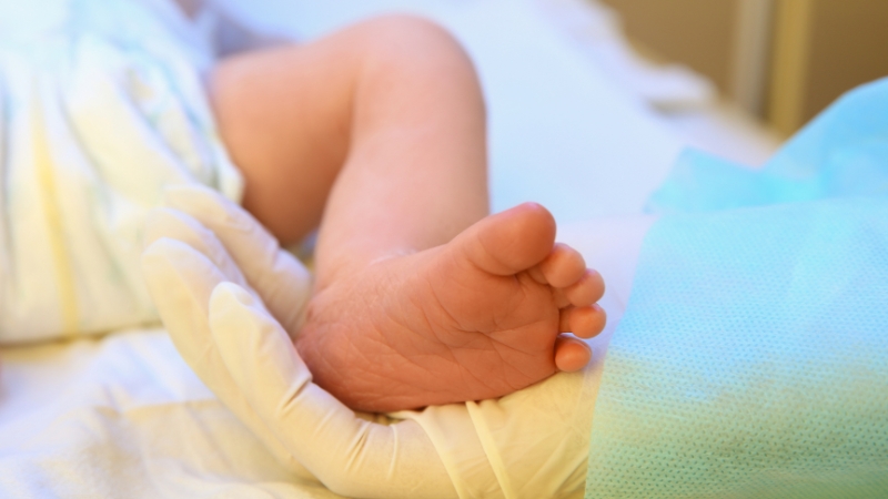 Doctor holding the tiny foot of a newborn baby in a hospital nursery