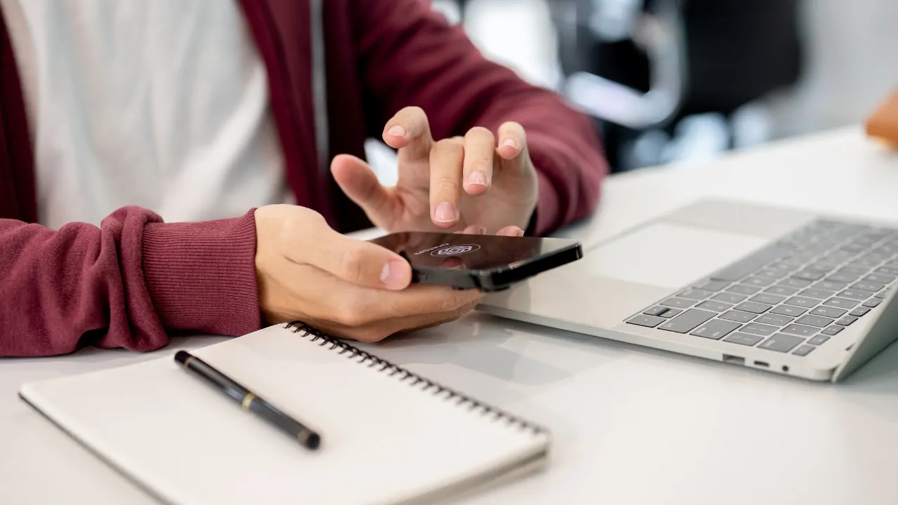 Student uses a phone and laptop for AI for school assignments at a desk