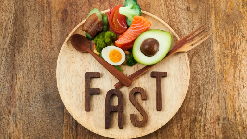Structured fasting plan with healthy foods arranged around the word FAST on a wooden plate