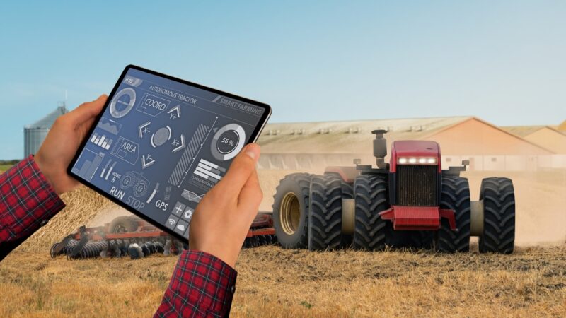 Farmer uses a tablet to control a tractor working in a harvested field