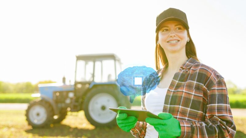 Farmer uses a tablet in a field with a tractor and AI icon in the background