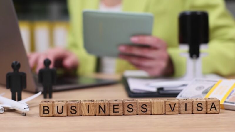 Person working on a laptop with “business visa” blocks placed on a desk in front