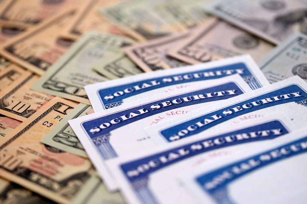 Close up of Social Security cards placed over US dollar bills, representing retirement benefits and COLA increases.