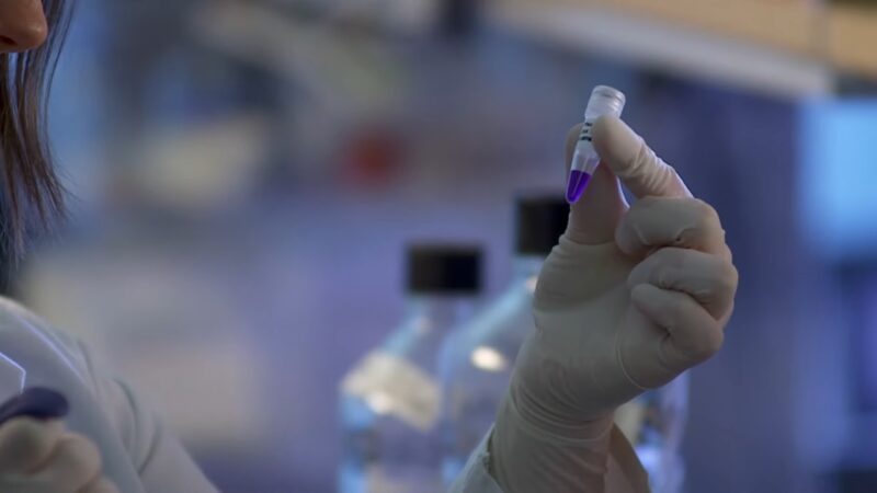 Researcher holding a small vial sample in a laboratory during drug testing
