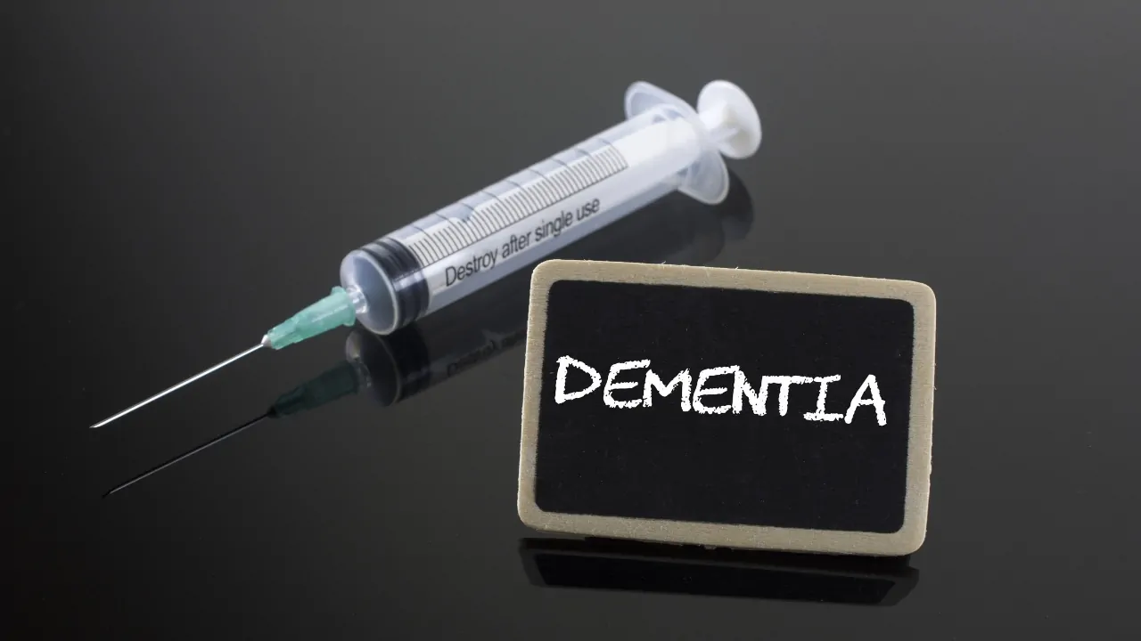 Dementia vaccine research concept with a syringe beside a small blackboard.