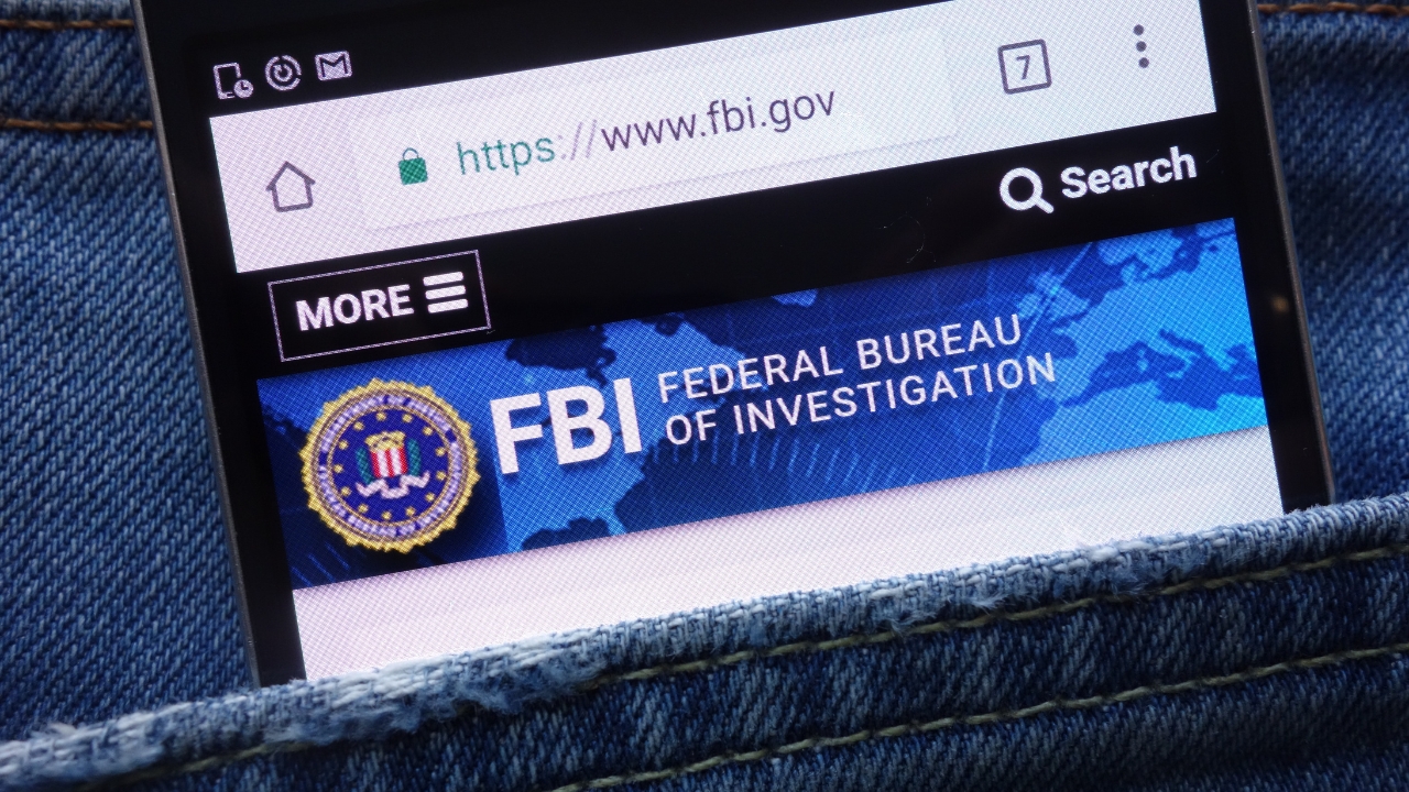 A phone shows the FBI website open in a browser