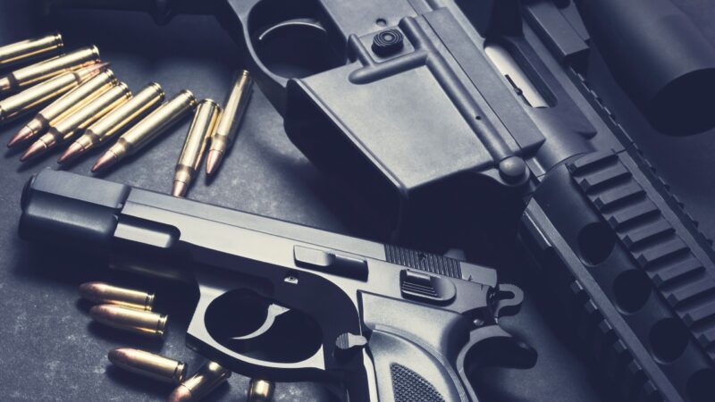 Handguns, rifle parts, and ammunition displayed on a dark surface
