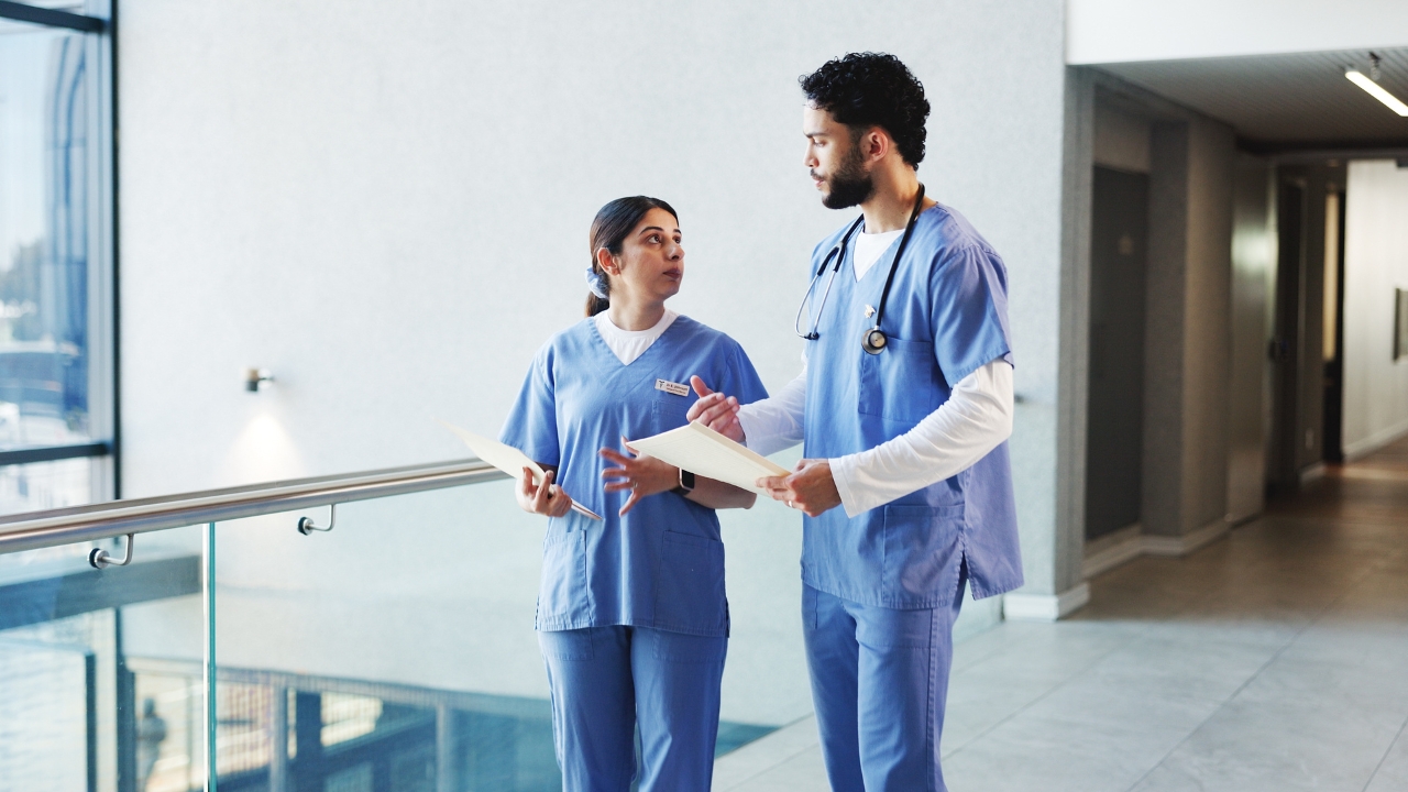 Two hospital workers discuss patient notes in a quiet corridor