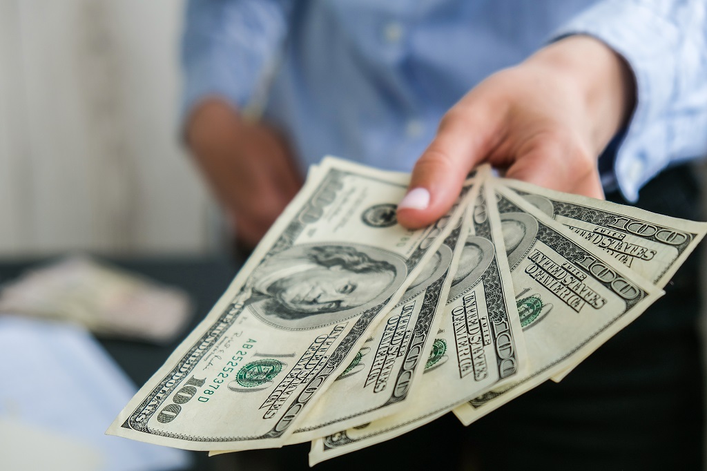 Close up of a person holding several one hundred dollar bills, representing financial contributions and long term savings for a child