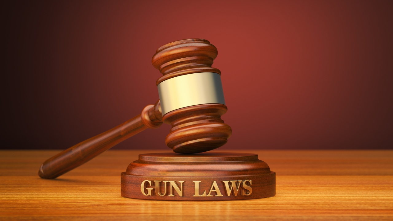 A judge’s gavel rests beside a “Gun Laws” sign on a wooden desk