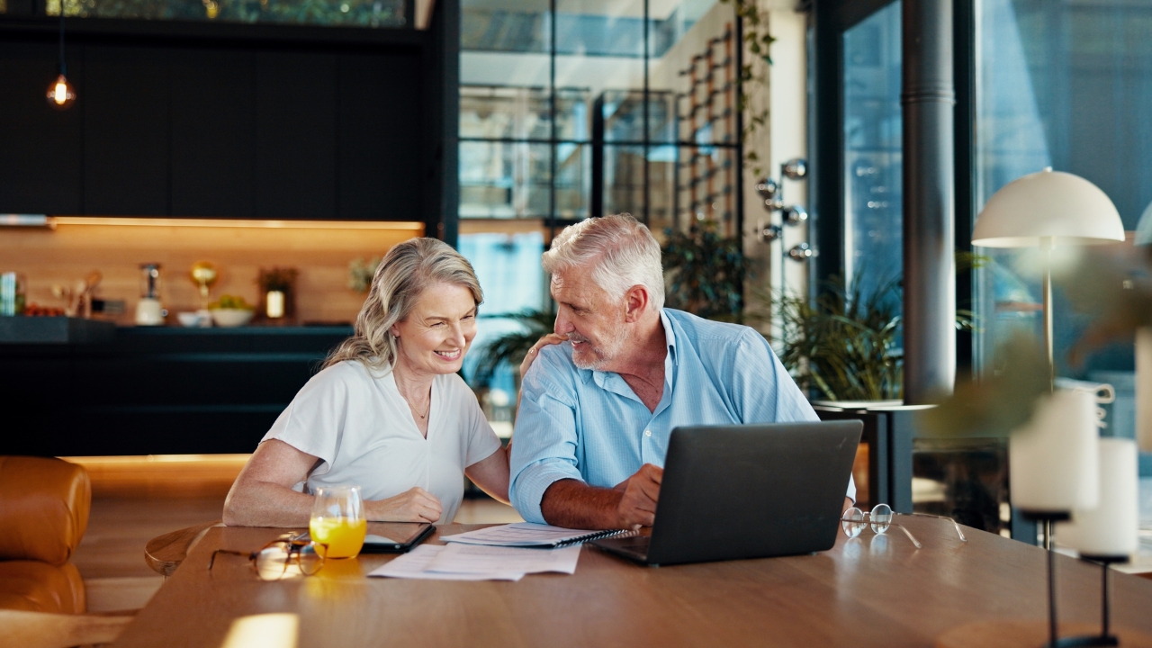 Older couple reviewing retirement papers on a laptop at home
