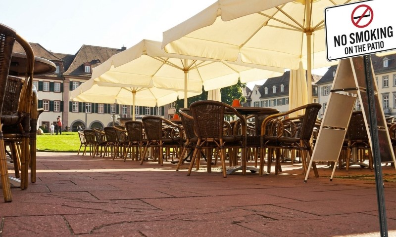 Outdoor patio seating with wicker chairs and tables under large beige umbrellas. A "No Smoking On The Patio" sign is visible