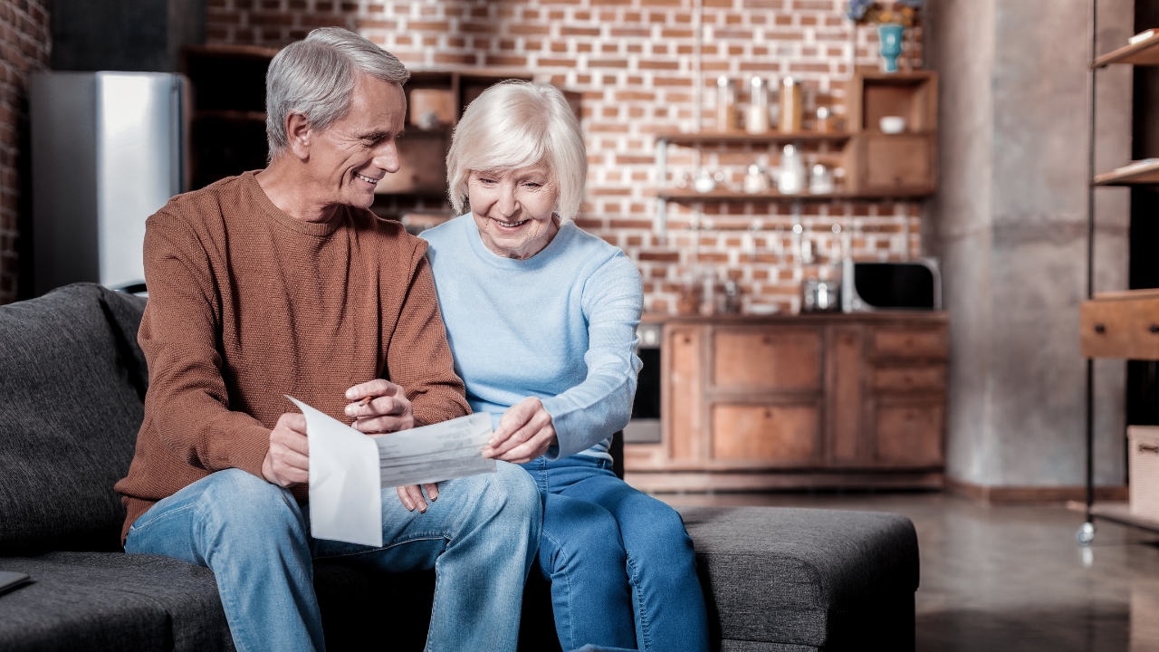 Retired couple sitting on a sofa and reading a Social Security check at home