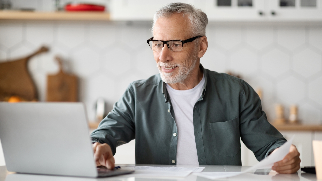 Older man reviews retirement papers on a laptop at home