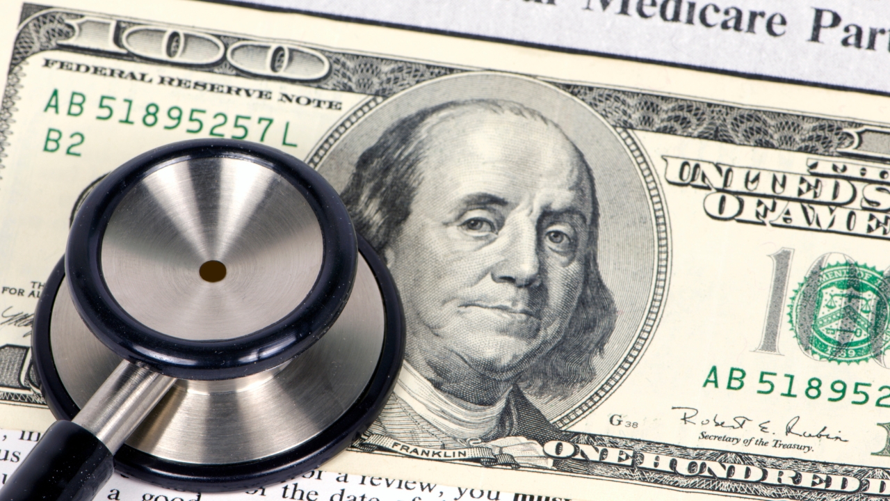 A stethoscope rests on a dollar bill beside Medicare paperwork