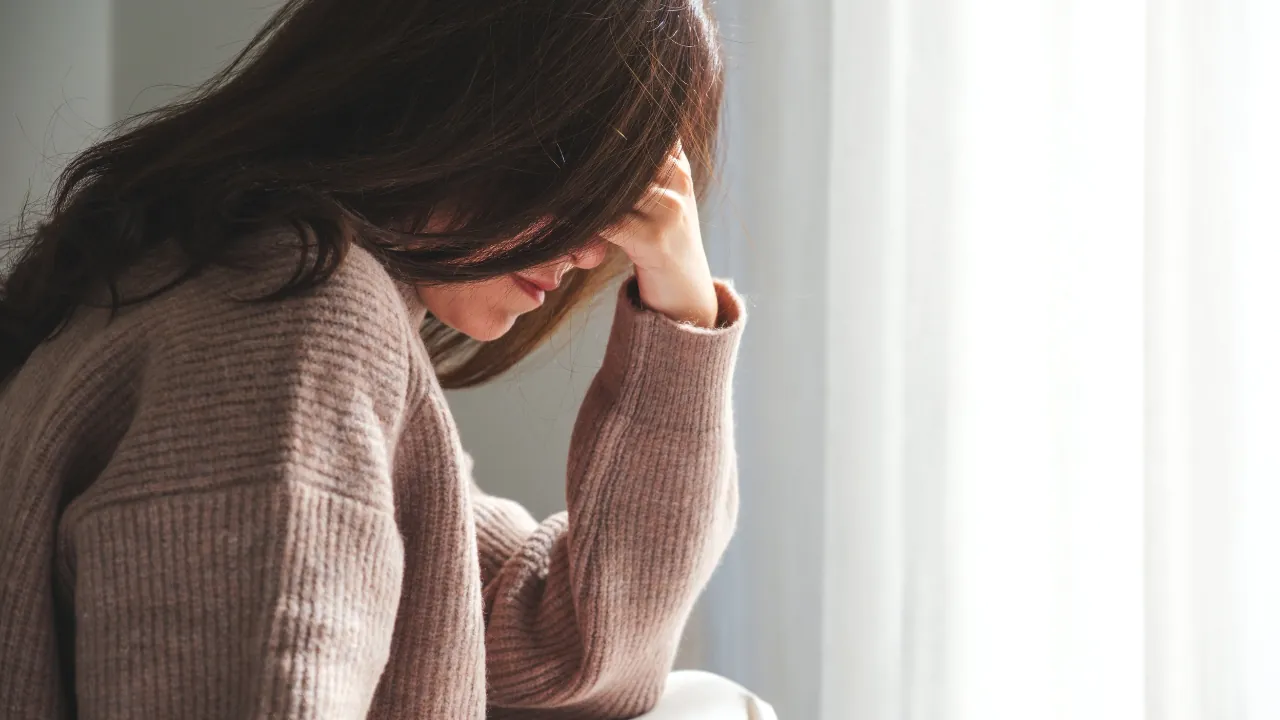 Woman sitting indoors with her head down, reflecting symptoms of anxiety or emotional stress