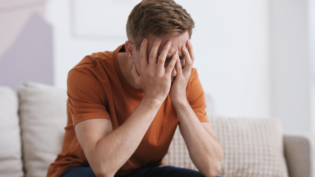 Man sits on a couch with his hands over his face